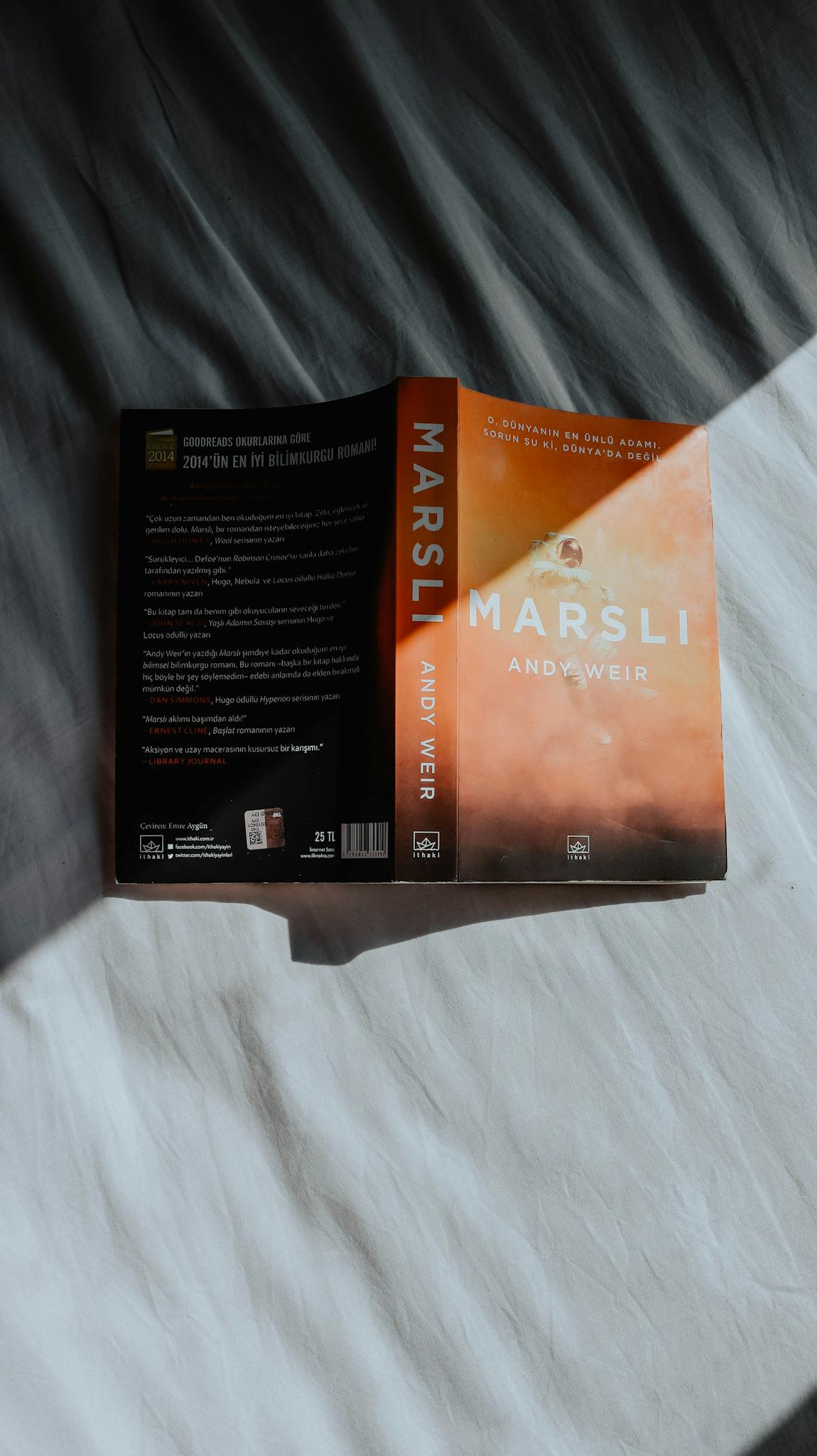 Open book 'Marsli' by Andy Weir on a fabric background, with natural light and shadows.